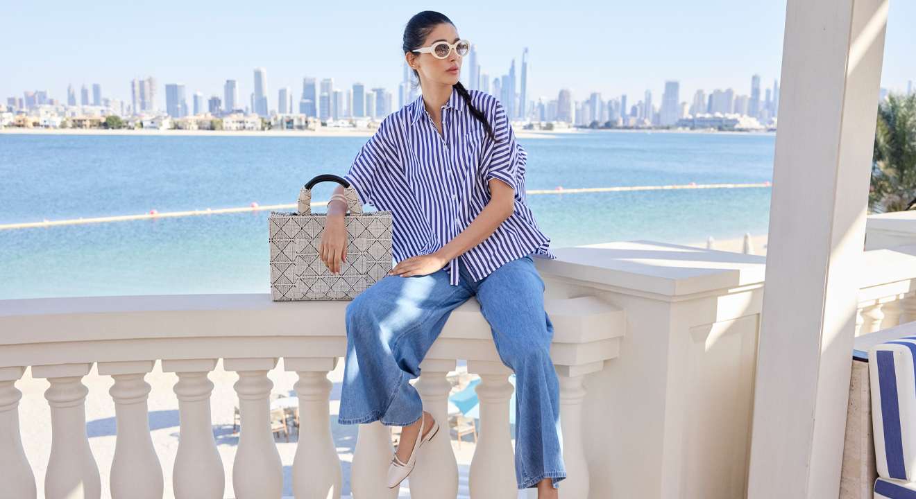 Frau in Marine-Look an Strandpromenade, sitzend auf Steingeländer, mit blau-gestreiftem Top