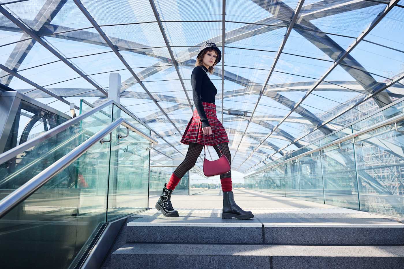 Frau in Punk Print-Outfit mit roter Handtasche am oberen Ende einer Treppe
