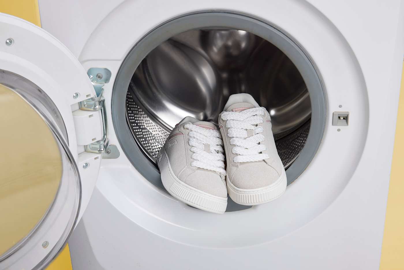 Weiße Schuhe stehen in offener Waschmaschine, bereit für den Waschgang