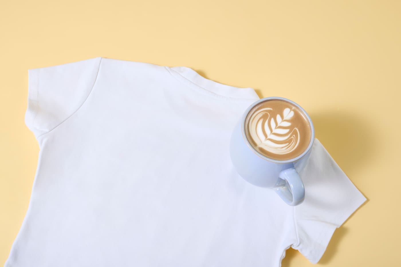 Tasse mit Kaffee steht auf weißem Shirt