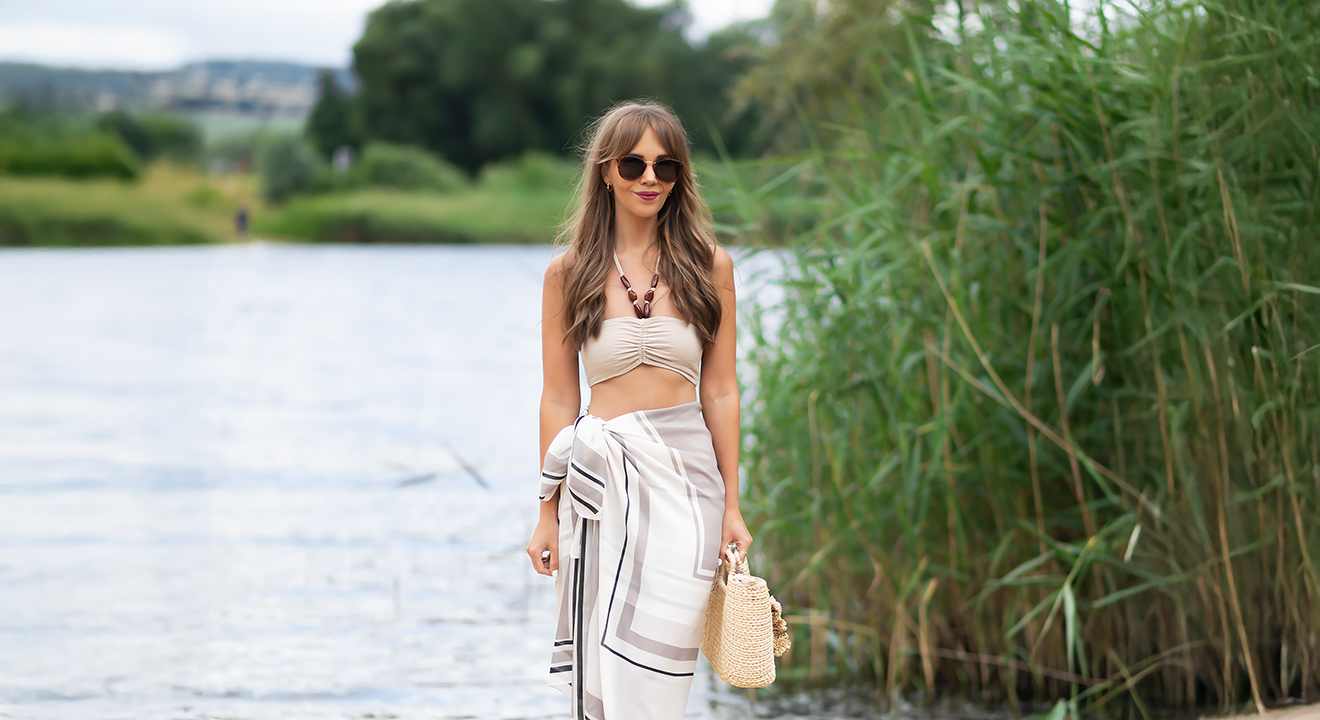Frau in luftigem Strandoutfit, stehend vor Seekulisse