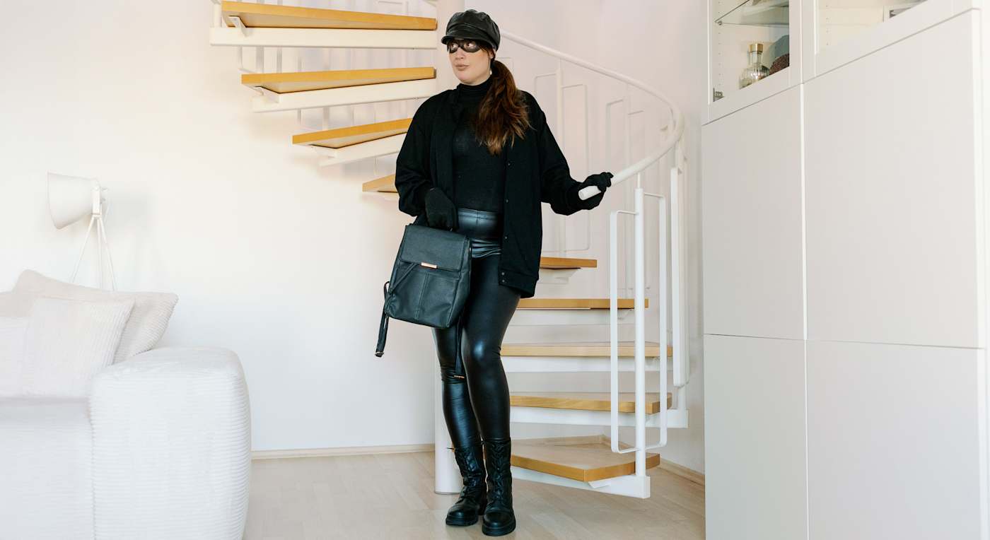 Frau gekleidet in Einbrecher-Karnevalskostüm, steht an Wendeltreppe