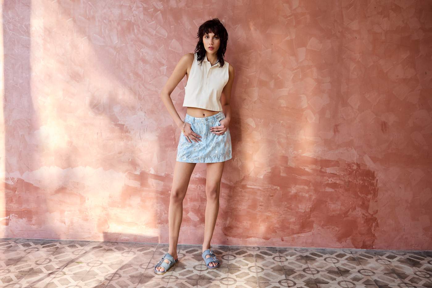 Frau in sandfarenem Top und Denim Rock, trägt zum Outfit Tieffußpantoletten