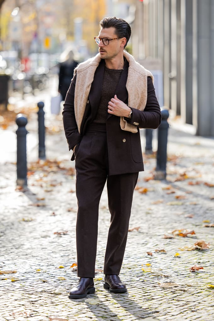 Mann in elegantem schwarzen Outfit, kombiniert Zweireiher mit warmem Rollkragenpullover über den Schultern