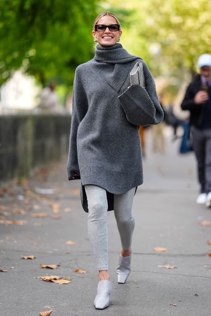 Frau in grauem Oversized-Sweater aus Strick und hellgrauen Yogapants, spazierend auf Boulevard