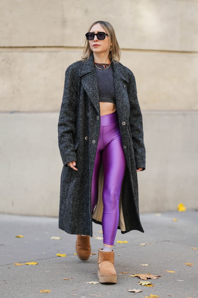Frau in Layering-Outfit, bestehend aus einem Longline-Coat, schwarzem Top und lilafarbener Yogapants samt Chunky Boots 