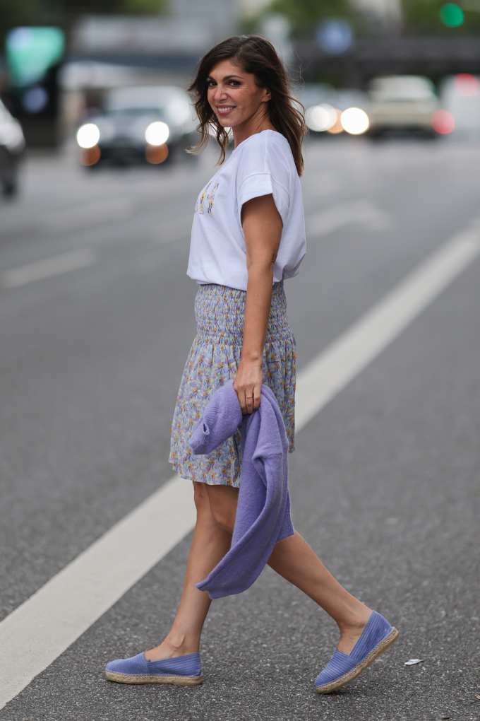 Frau in Casual-Look, mit weißem Top, Rock und Espadrilles, spaziert über eine Straße