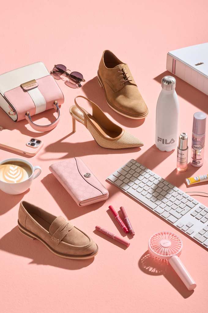 Sammelsurium aus Business-Schuhen sowie Tastatur, Handy, Tasche und Co. auf rosa Oberfläche