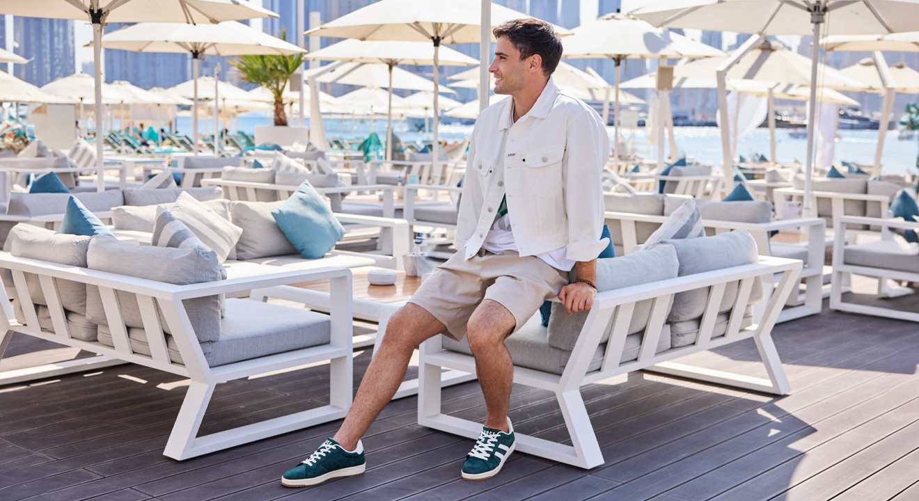 Mann in lässig-weißem Outfit, lehnt an einer weißen Bank in einer Strandbar