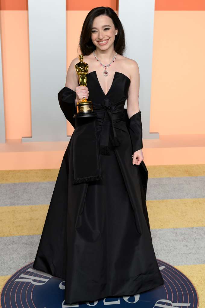 Mikey Madison posiert in einem eleganten schwarzen Abendkleid mit einem Oscar und einer auffälligen Halskette vor einem stilvollen Hintergrund