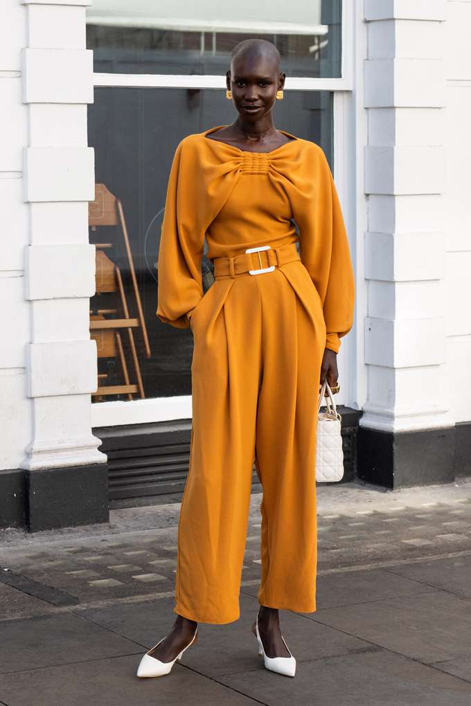Dunkelhäutige Frau in stark kontrastierendem Jumpsuit in Orange, mit weißen High Heels