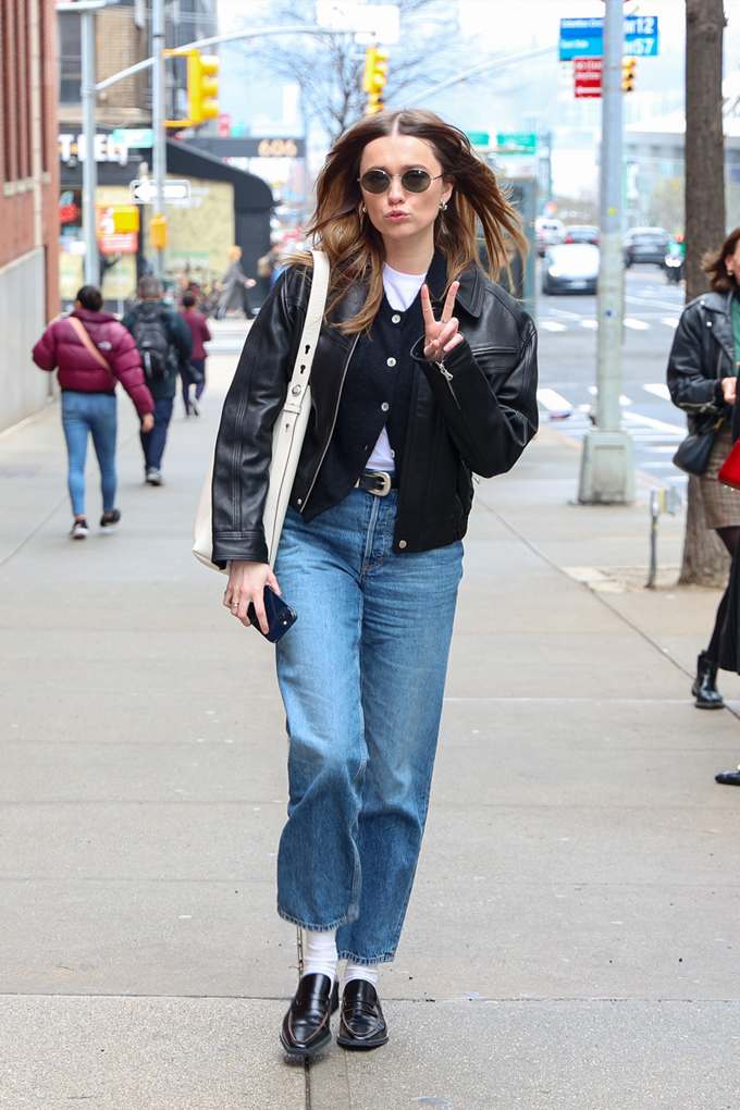 Schauspielerin Aimee Lou Wood auf Straße mit Outfit aus Jeans, Cardigan und schwarzer Lederjacke