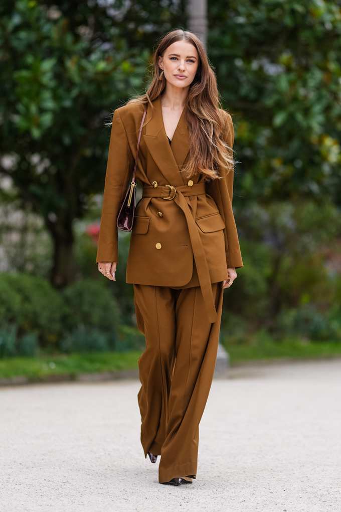 Frau mit Office Siren-Outfit in Kaffeebraun mit goldenen Knöpfen und Gürtel 