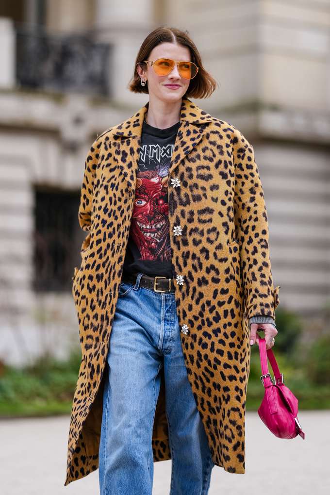 Frau trägt Leopardenmantel, kombiniert mit Bandshirt und Denim-Jeans, laufend auf Straße