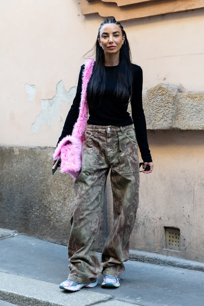 Frau mit schwaruem Top und Baggy Pants in Camo-Optik, kombiniert mit pinker Plüschtasche