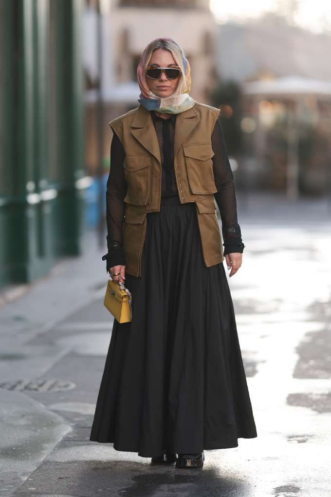 Frau mit brauner Anglerweste im Utility Style, kombiniert mit schwarzer Bluse, Maxirock und Kopftuch