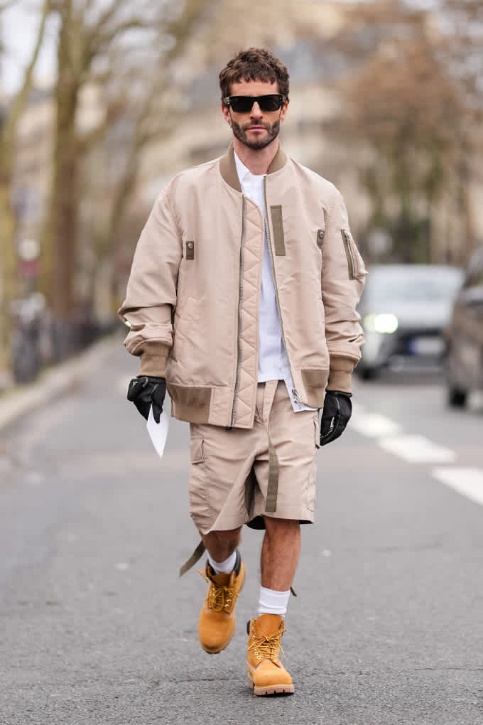 Mann in beiger Bomberjacke mit Utility-Shorts und dicken Boots