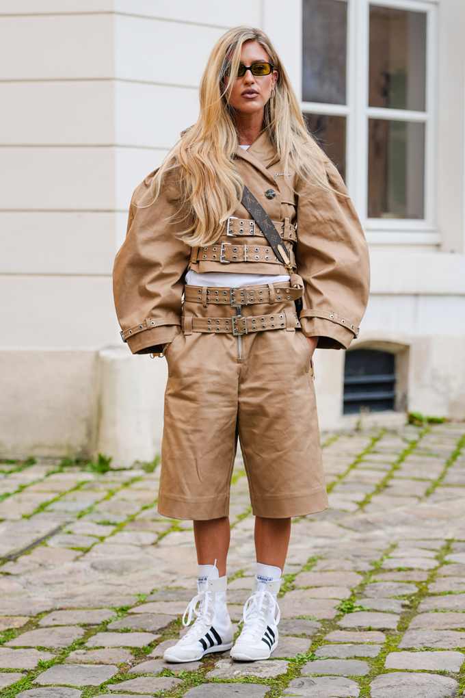 Frau trägt beigen Cropped Trenchcoat, kombiniert mit Knie-Shorts und Sneaker-Schuhen