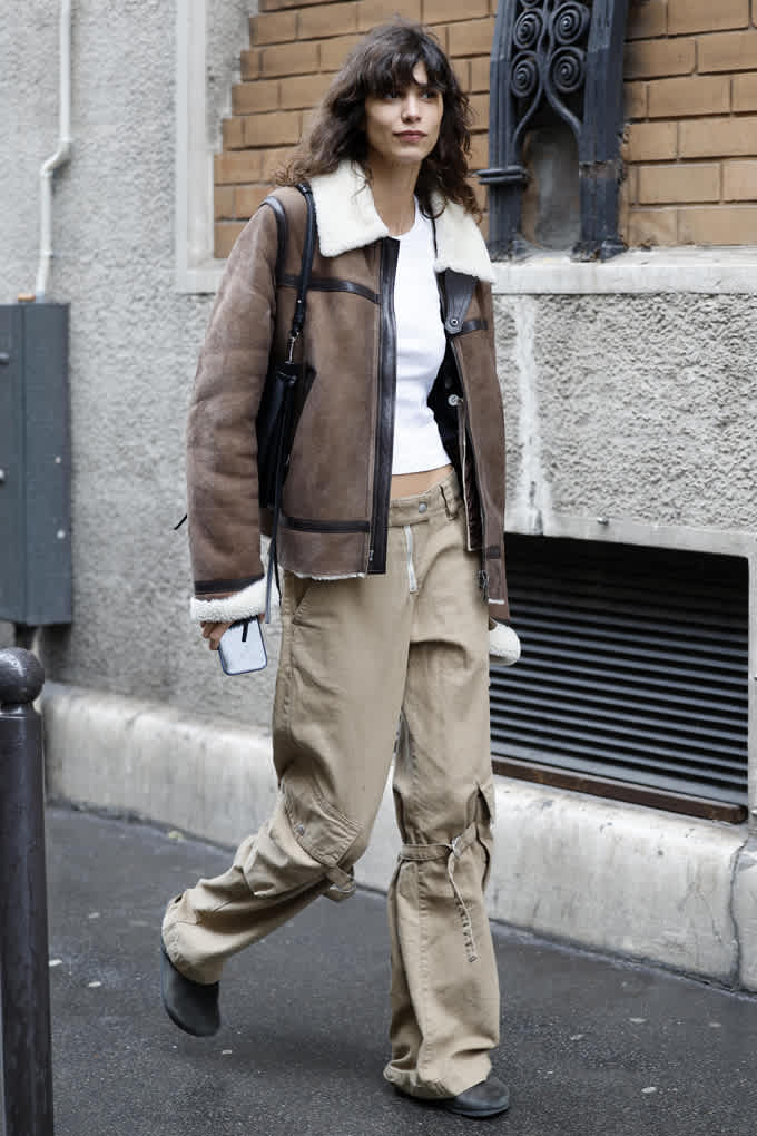 Frau mit brauner Teddy-Bomberjacke und weißem Top mit Techno-Cargopants
