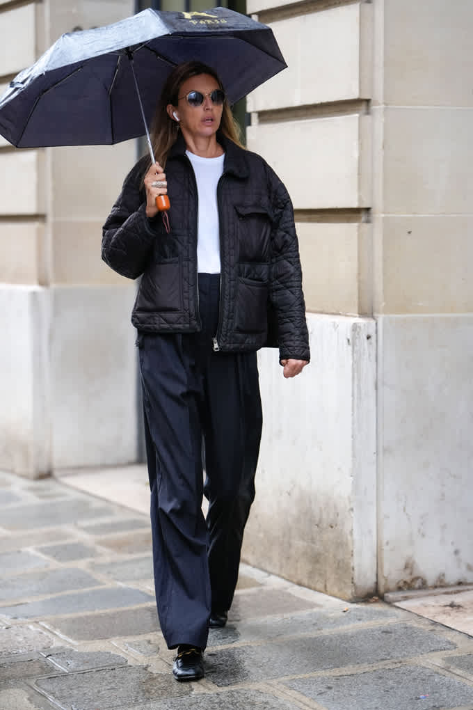 Frau mit blauer Steppjacke und Oversize-Suitpants, hält Regenschirm in der Hand