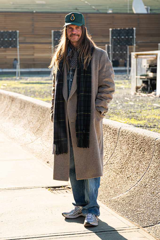 Mann in lässigem Outfit mit Oversize-Mantel, Jeans und grüner Basecap