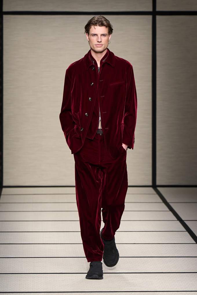 Ein junger Mann ist auf einem Catwalk, er trägt einen dunkelroten Samtanzug