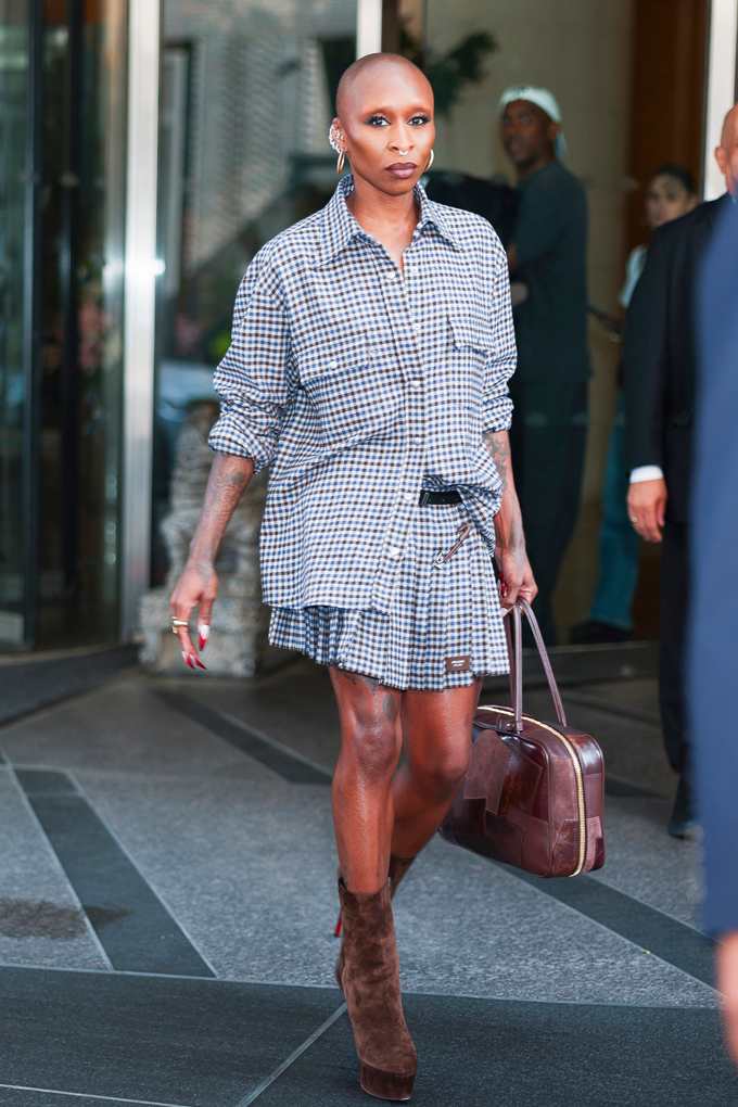 Cynthia Erivo trägt einen Rock und ein Hemd mit demselben karierten Muster, in ihrer Hand trägt sie eine braune Tasche