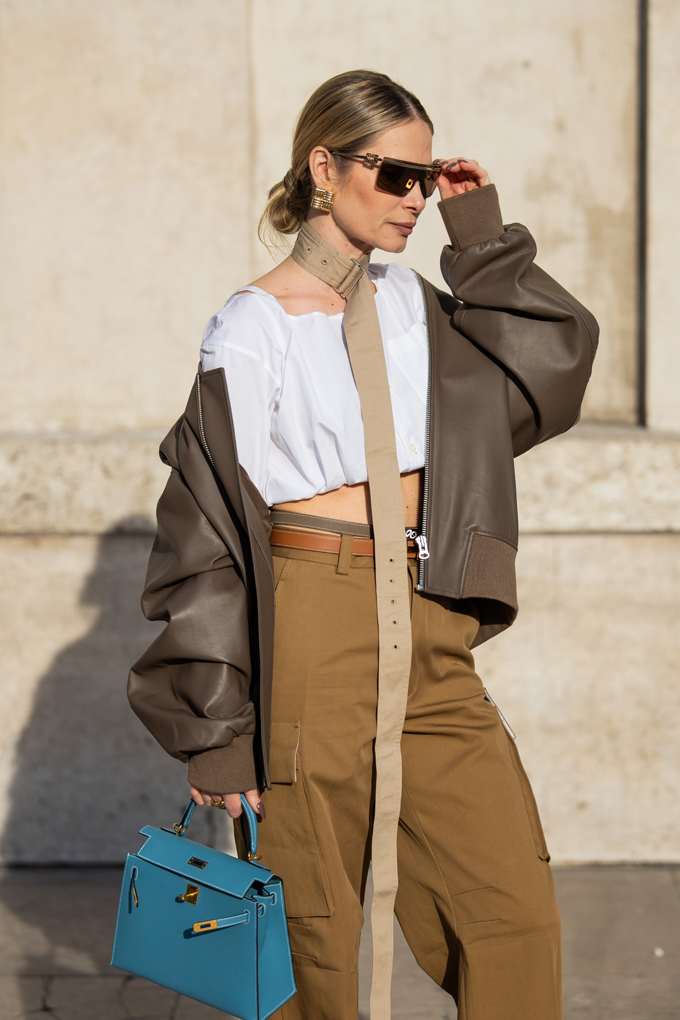 Frau in olivfarbenem Leder-Blouson, mit weißer Hemdbluse und passender Bundfaltenhose