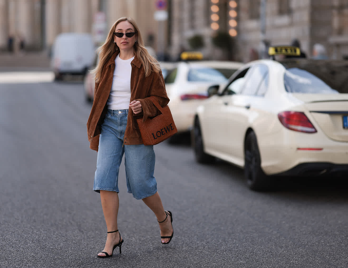 Frau in braunem Shacket, Jeans-Shorts und Heels, spaziert über Straße