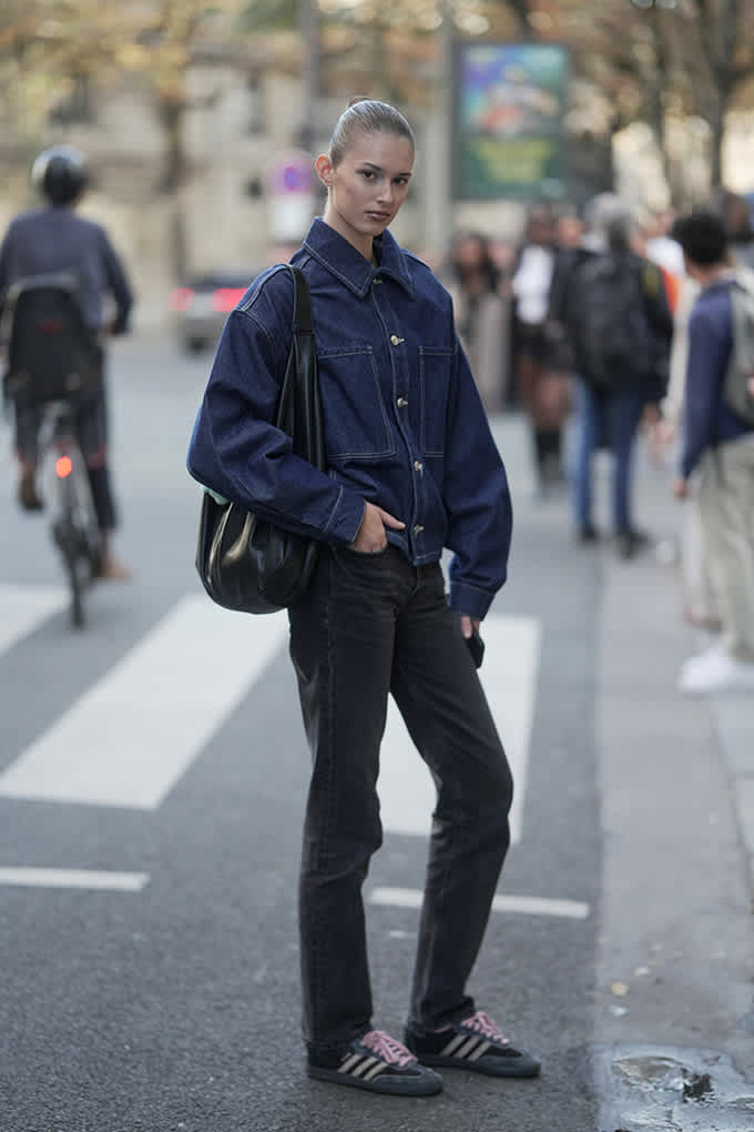 Frau posiert auf Straße, trägt übergroße Jeansjacke in Denim mit Handtasche