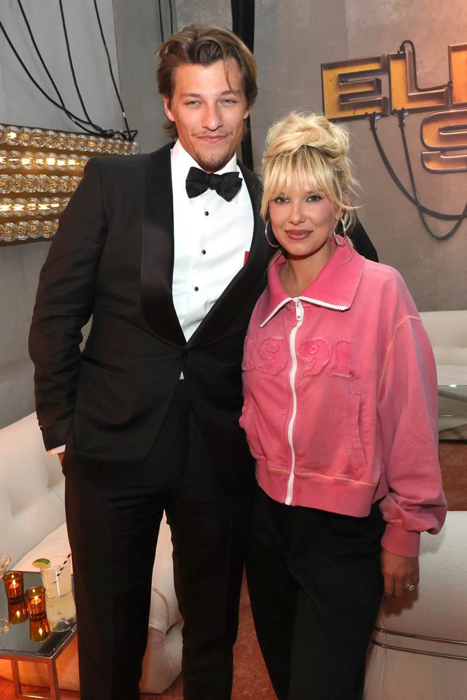 Star-Ikone Millie Bobby Brown, in pinkem Blazer, posiert neben Kollegen im Anzug