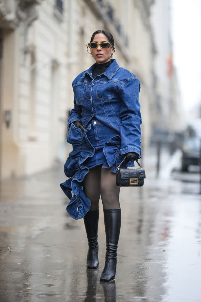 Frau in dunkelblauer Jeansjacke, spaziert auf regennassem Gehweg. trägt schwarze Handtasche in der Hand