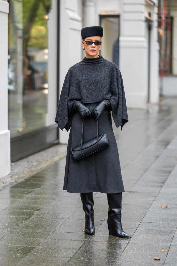 Frau trägt elegant-schwarzes Outfit, kombiniert mit passender Kopfbedeckung und Baguette Bag