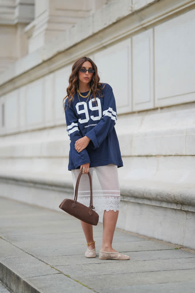 Langhaarige Frau trägt blaues College-Shirt in Kombination mit Minirock und Handtasche