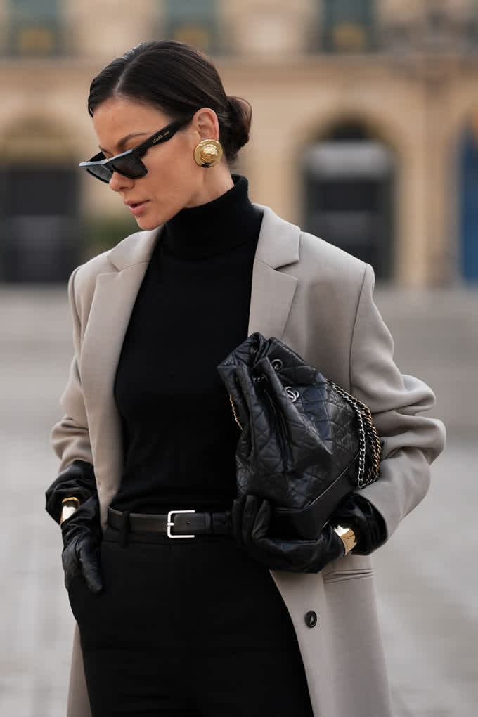 Frau trägt schwarzen Turtleneck-Pullover mit grauem Blazer und schwarzer Handtasche