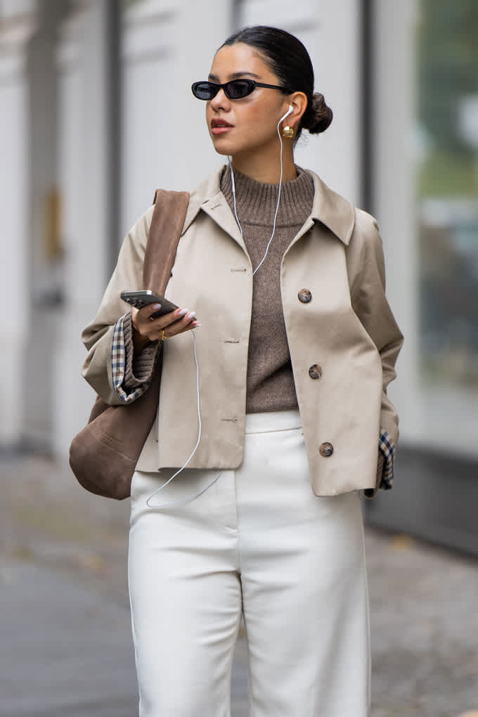 Frau trägt elegantes Outfit, bestehend aus dunkelgrauem Turtleneck-Pullover, kombiniert mit beigem Blazer und Handtasche am Arm
