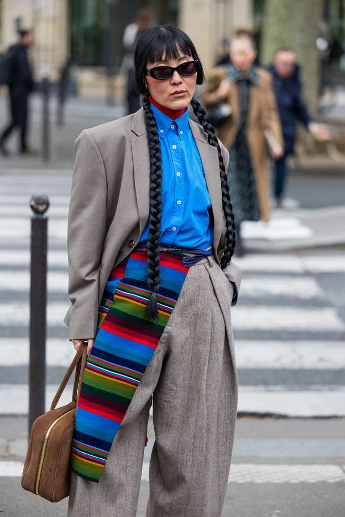 Frau in grauer Blazer-Kombination, trägt blaues Hemd dazu, in urbaner Umgebung
