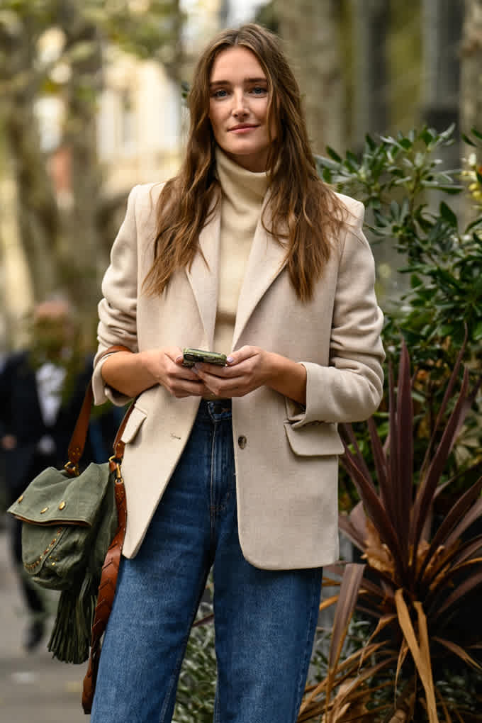 Frau mit schulterlangem Haar trägt beigen Blazer mit passendem Turtleneck und blauer Jeans