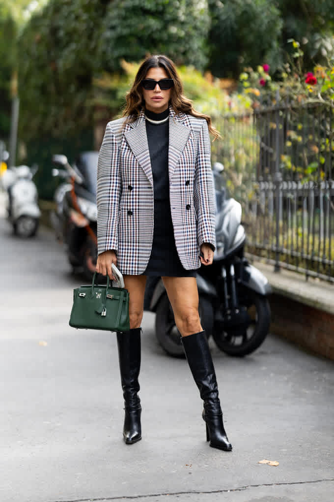 Frau mit großer Sonnenbrille, trägt karierten Blazer über schwarzem Kleid, kombiniert mit Underknee Boots