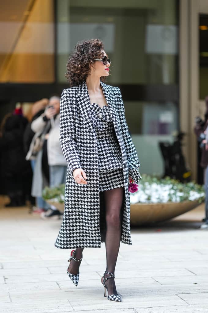 Frau mit lockigen Haaren trägt Mantel in Karo-Muster in Kombination mit identisch gemustertem Kleid und Schuhen