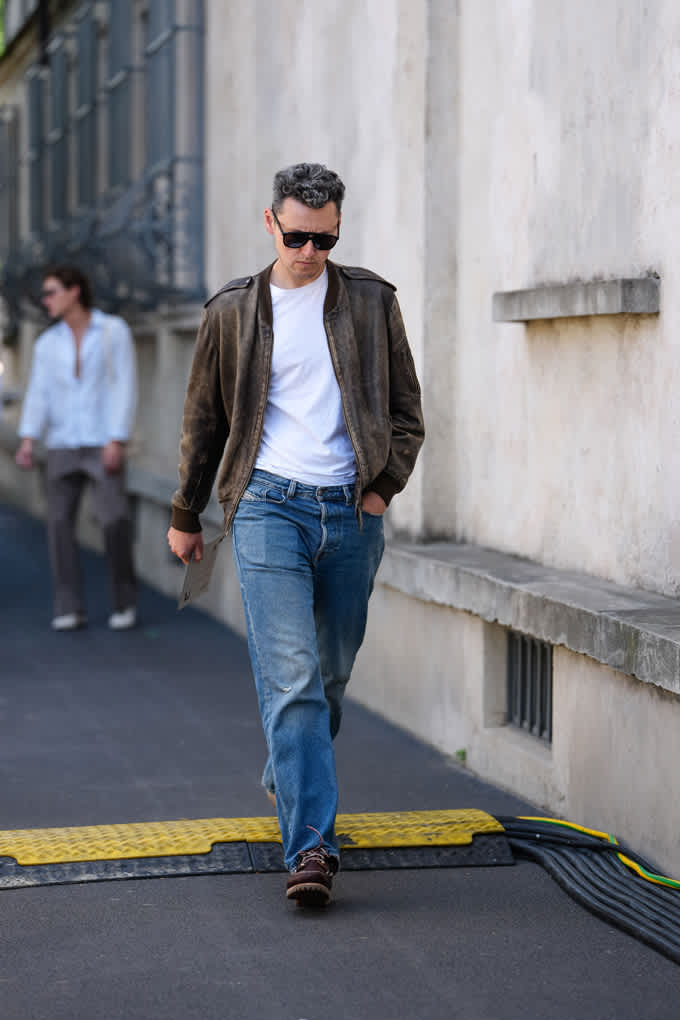 Mann in Rockabilly-Style-Outfit spaziert auf Gehweg, trägt braune Jacke mit weißem Shirt Denim-Hose
