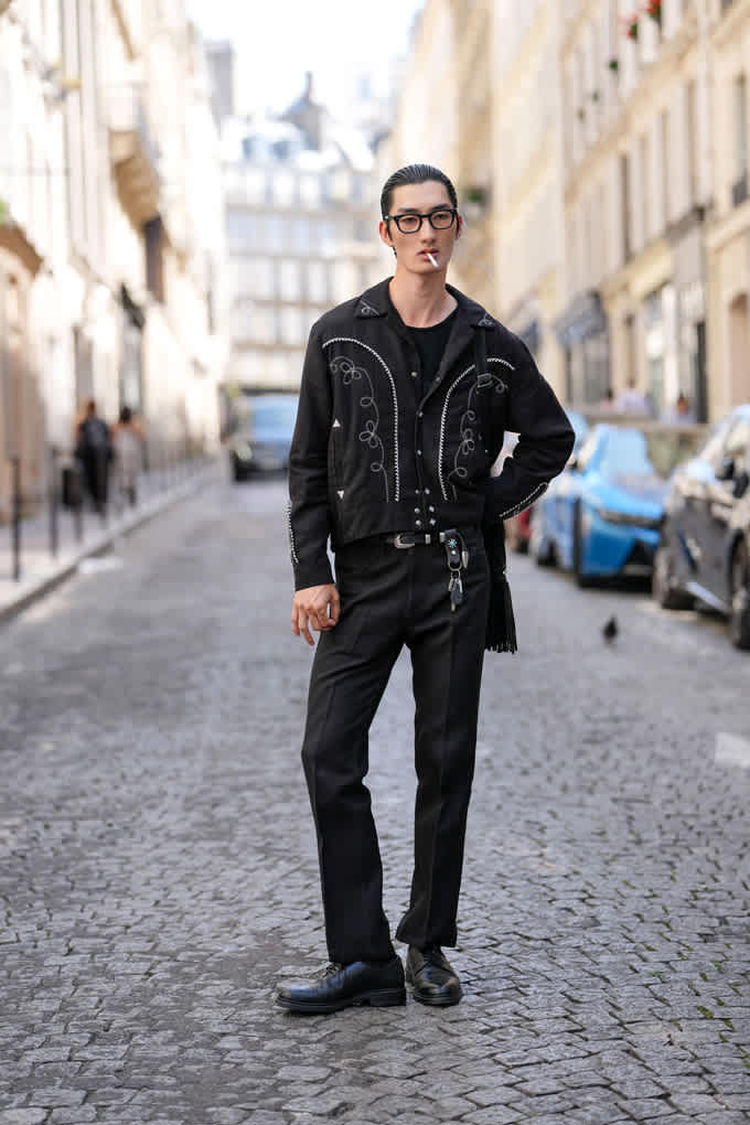 Mann trägt schwarzes Leder-Outfit im Rockabilly-Look, steht auf Pflastersteinstraße zwischen Häusern