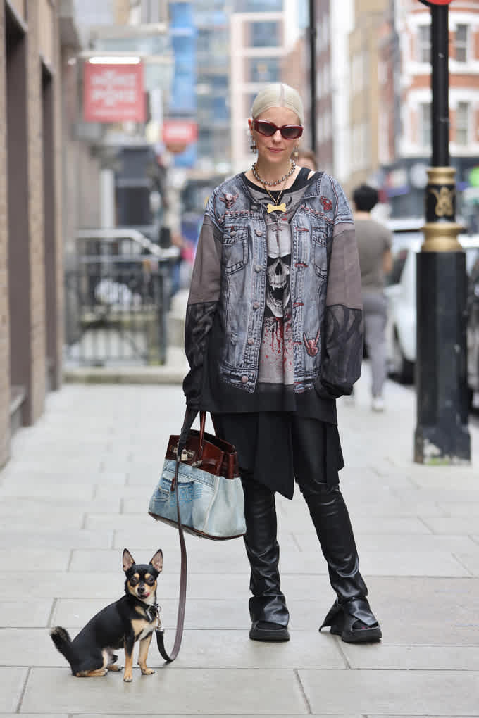 Frau in hellgrauem Grunge-Look, steht auf Bürgersteig, mit Handtasche und Hund an Leine