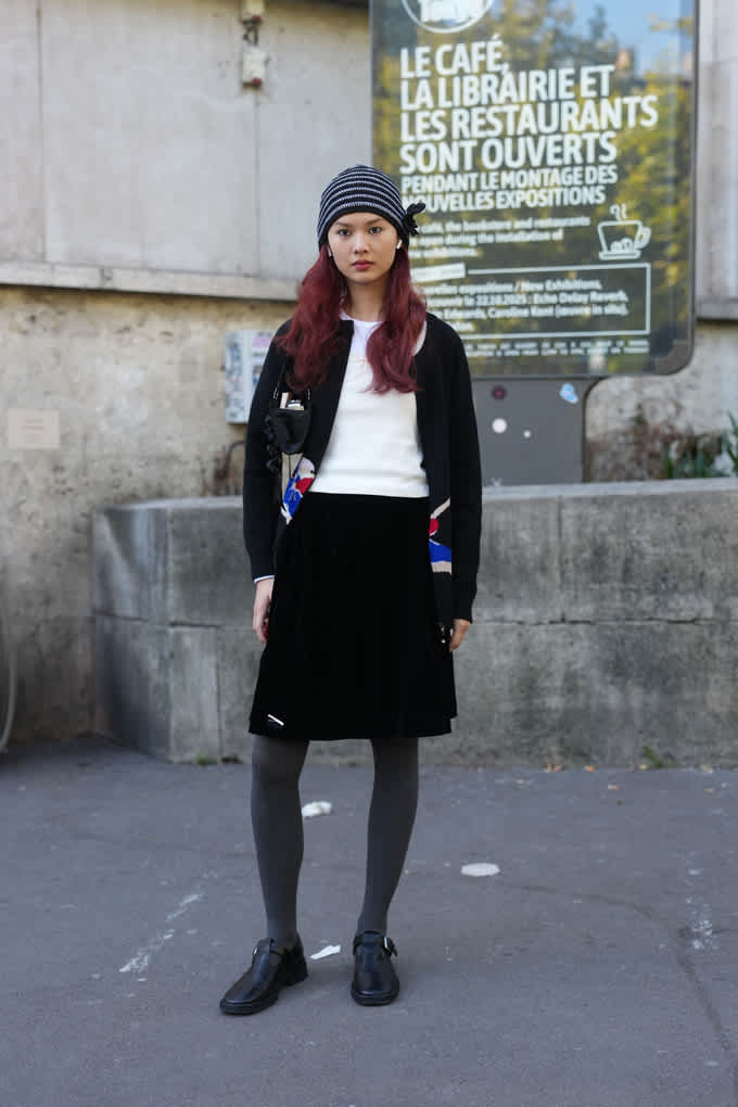 Junge Frau trägt Strickmütze, Faltenrock und Strickcardigan, stehend vor Steintreppe