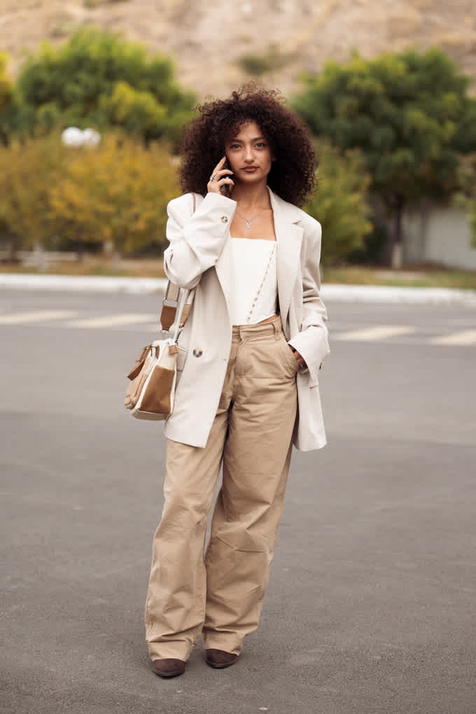 Schwarzhaarige Frau mit Creme-Blazer, passendem Top und sandfarbenen Utility Pants