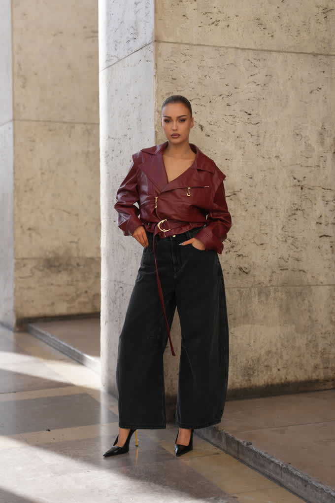Frau posiert in Sleek Look-Outfit mit burgunderfarbener Lederjacke und Wide Leg-Pants in Schwarz