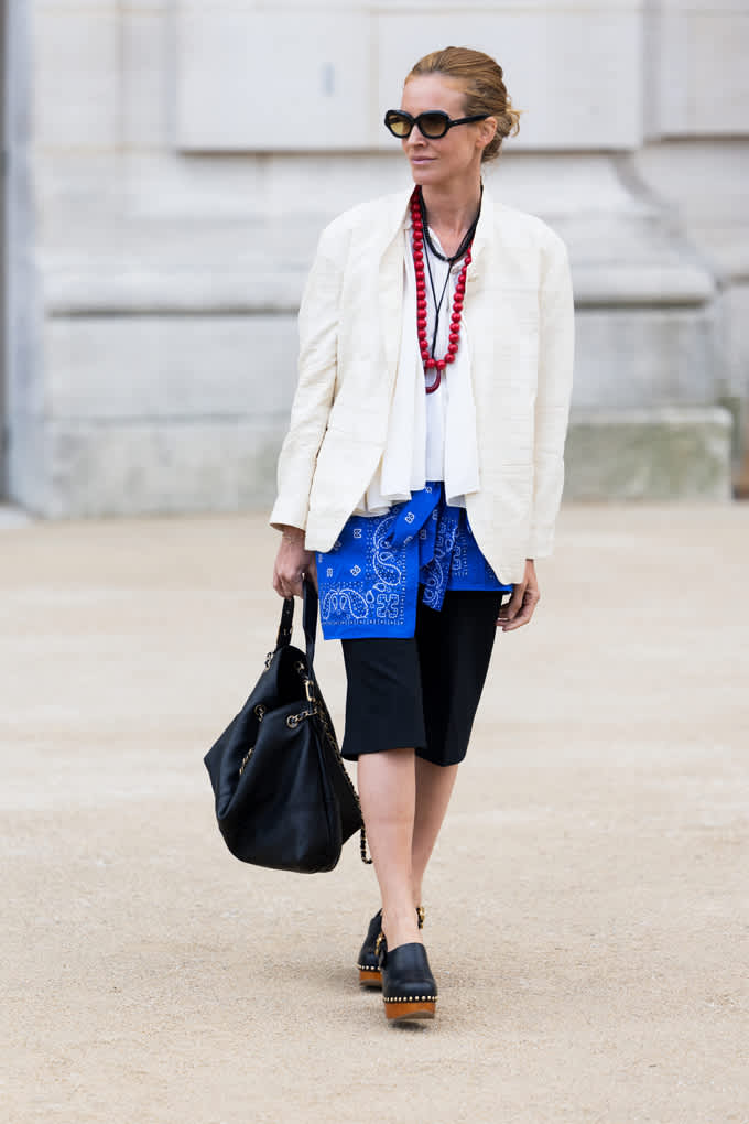 Frau trägt hellen Blazer über weißer Bluse, dazu ein blaues Bandana und Holzclogs, ganz im Layering-Style