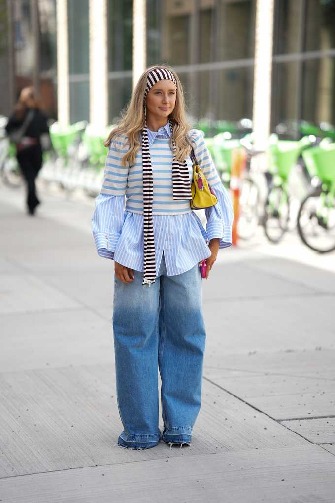 Frau steht auf Gehweg, trägt Streifen-Top und -Schal über hellblauem Hemd und Wide-Leg-Jeans