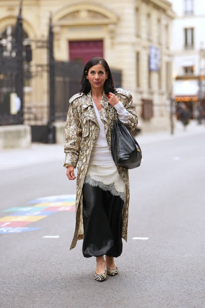 Frau spaziert in Snakeprint-Trenchcoat über beigem Top, kombiniert mit schwarzer Handtasche