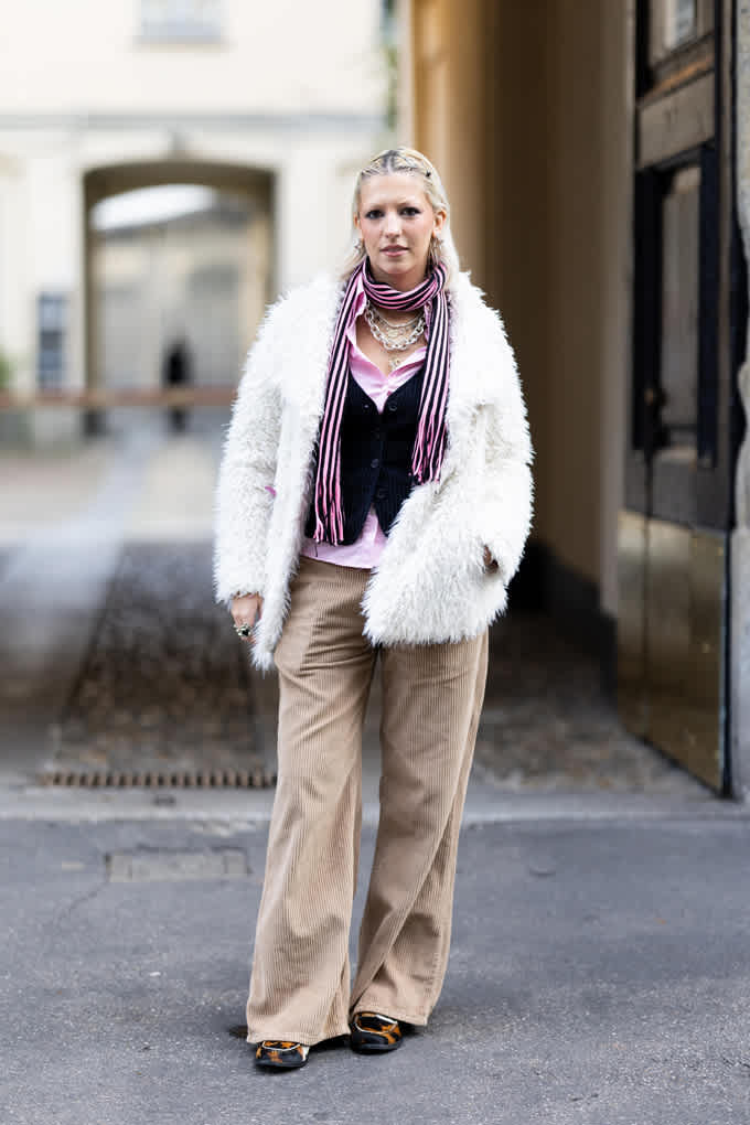 Frau in Layering-Outfit, trägt lila Top unter Weste und Faux Fur-Jacke